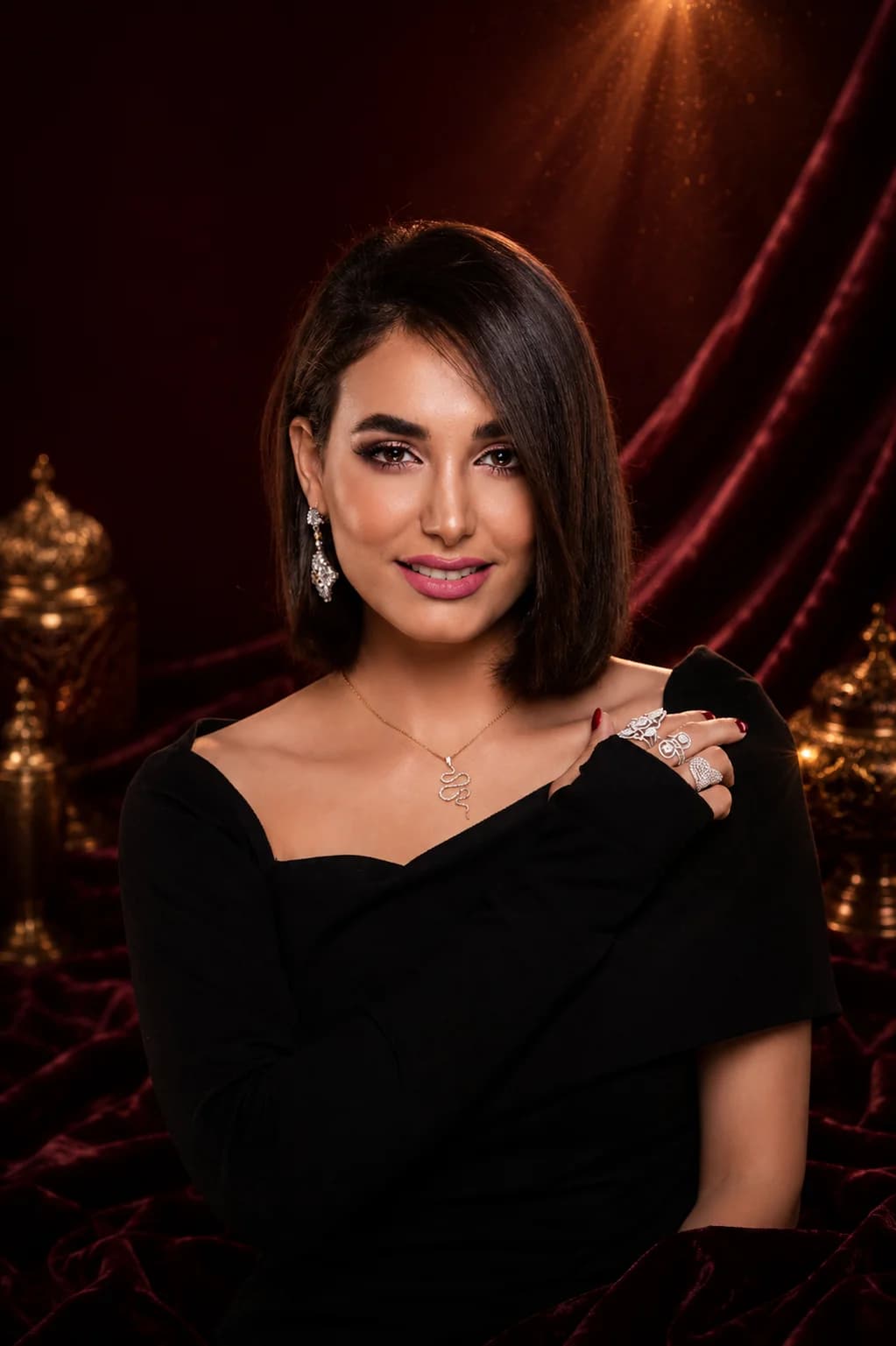 Model wearing drop earrings, a necklace, and rings against a maroon velvet backdrop