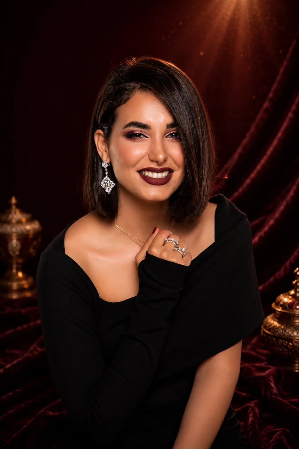 Model wearing earrings, a necklace, and rings against a maroon velvet backdrop